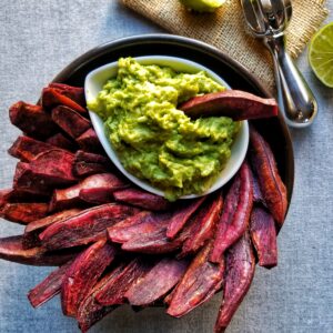 purple sweet potato wedges in a black bowl with guacamole