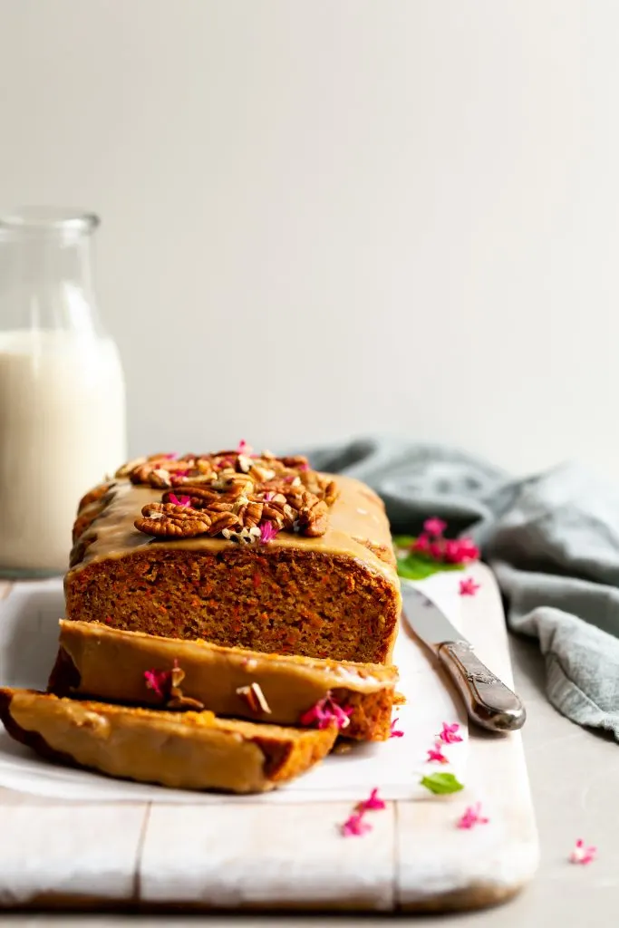 Vegan Carrot Spice Loaf with Maple Glaze with 2 slices cut and garnished with pink currant blossoms