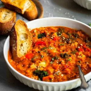 White bowl of roasted vegetable stew with red lentils and tomatoes, served with a thick slice of toast