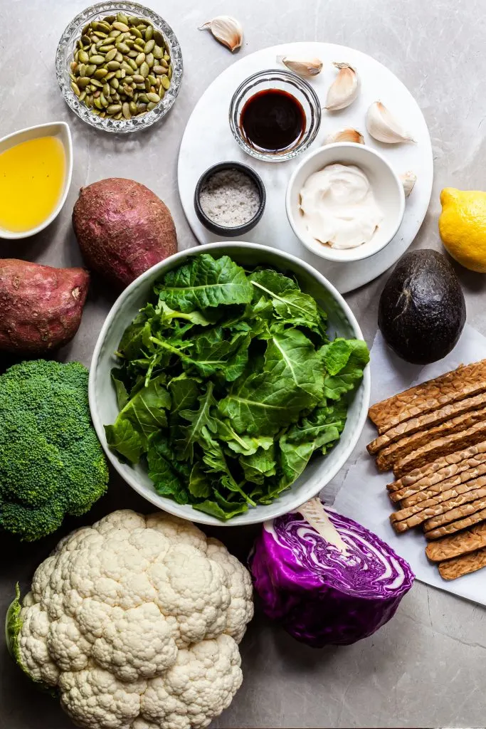 Flat lay of the ingredients used in this roasted vegetable salad and caesar dressing incluidng potatoes, cauliflower, brocolli, tempeh bacon, avocado, garlic and others