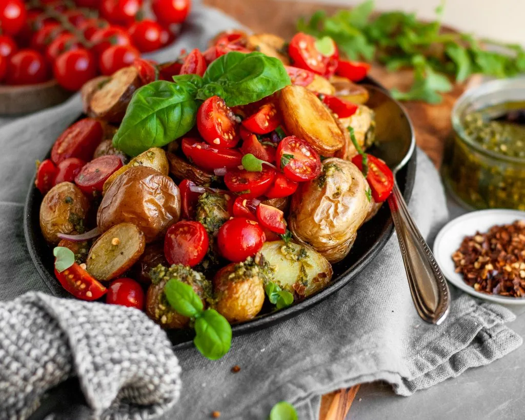 Roasted Baby Potatoes with Basil Pesto and Cherry Tomato Bruschetta being served with extra pesto and chili flakes