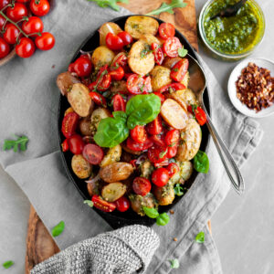 Roasted Baby Potatoes with Basil Pesto and Cherry Tomato Bruschetta being served with extra pesto and chilil flakes