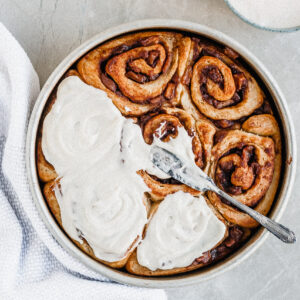 Vegan Apple Cinnamon Rolls being slathered with Vanilla Glaze