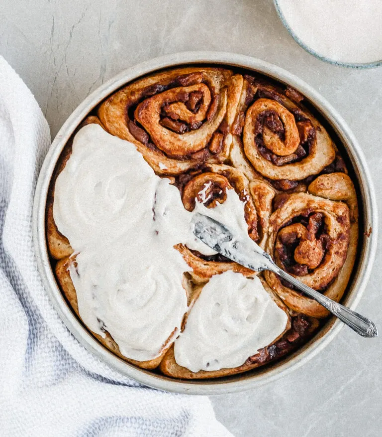 Vegan Apple Cinnamon Rolls being slathered with Vanilla Glaze