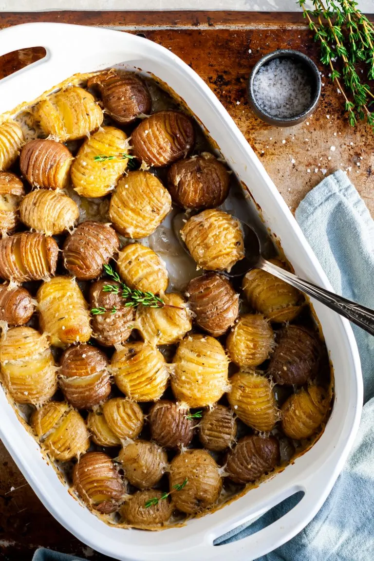 white casserole dish with baby hasselback potatoes in a creamy sauce