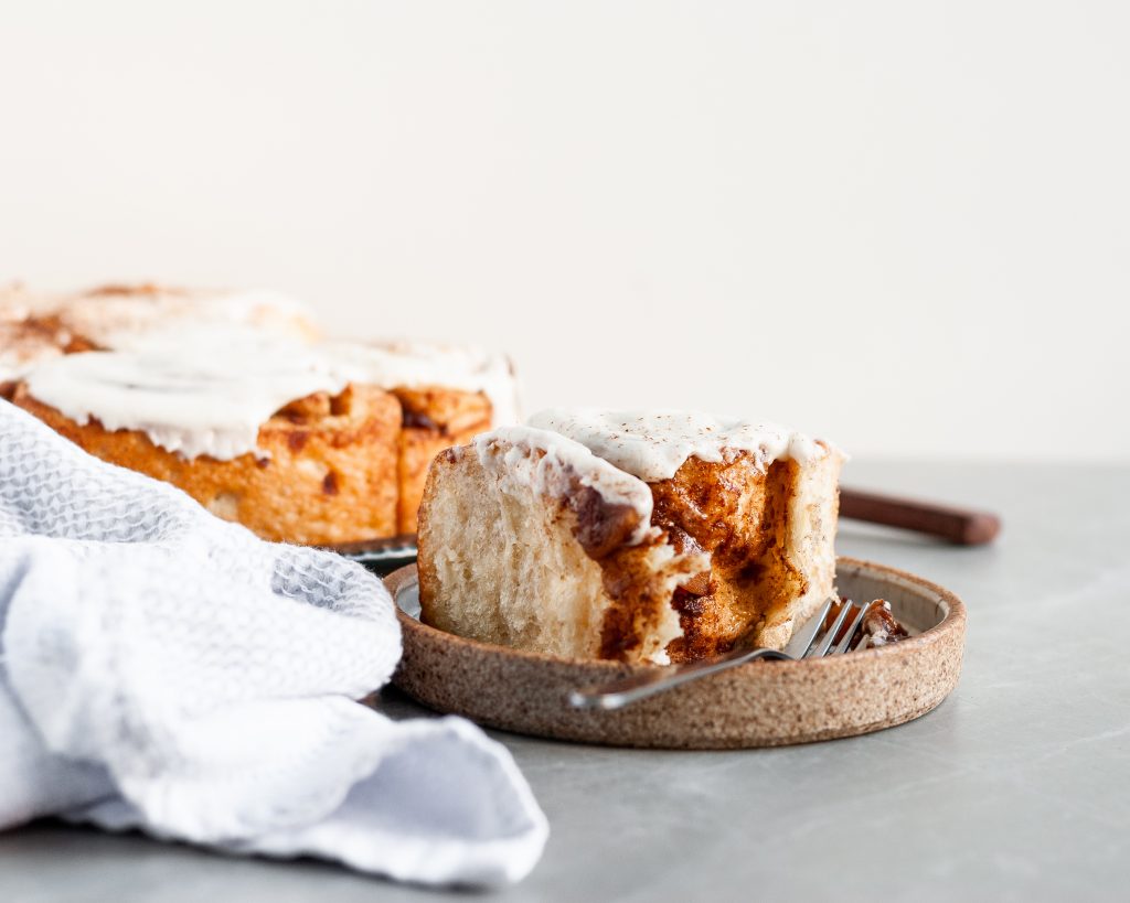 Apple Pie Cinnamon Roll topped with Vanilla Glaze with a single bite take out of it