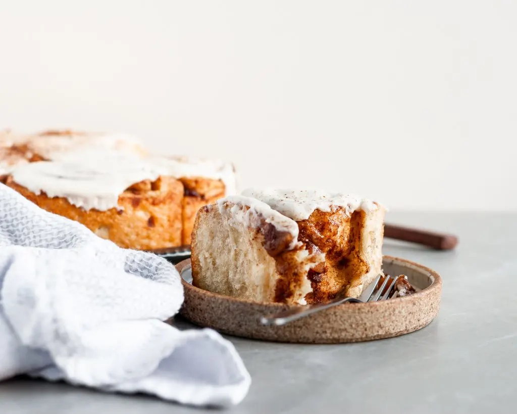Apple Pie Cinnamon Roll topped with Vanilla Glaze with a single bite take out of it
