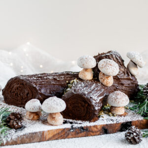 Vegan Chocolate Yule Log with Meringue Mushrooms served on a plank covered in icing sugar "snow"