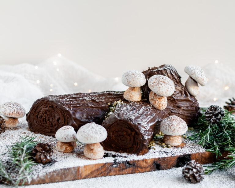 Vegan Chocolate Yule Log with Meringue Mushrooms served on a plank covered in icing sugar "snow"