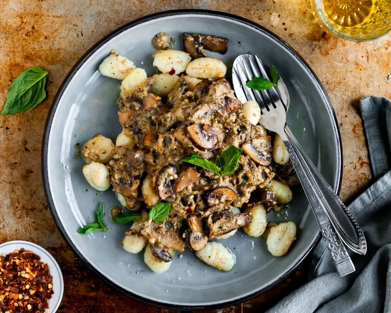 Plate filled with Pan-Fried Gnocchi and Seared Mushrooms in a Cashew Butter Pesto Sauce served with chilli flakes, fresh basil