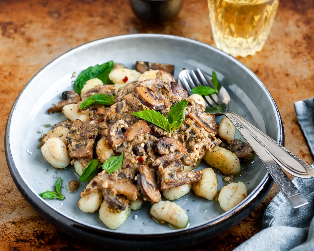 Plated Pan-Fried Gnocchi and Seared Mushrooms in a Cashew Butter Pesto garnished with fresh basil