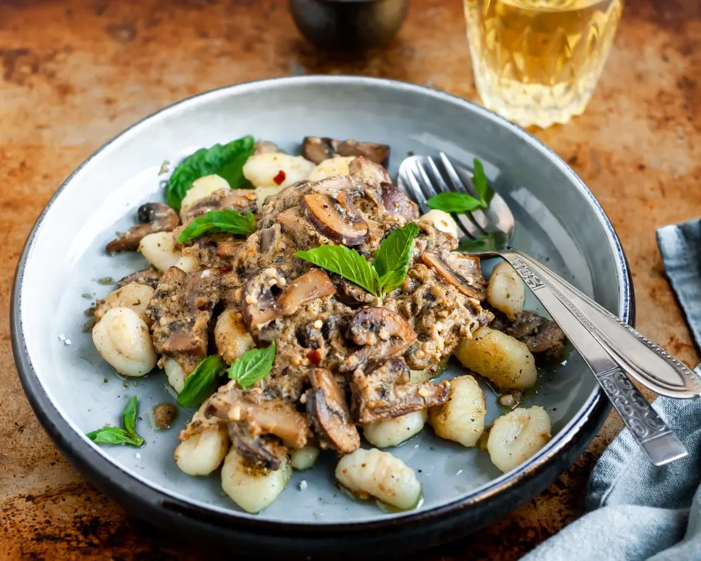 Plated Pan-Fried Gnocchi and Seared Mushrooms in a Cashew Butter Pesto garnished with fresh basil