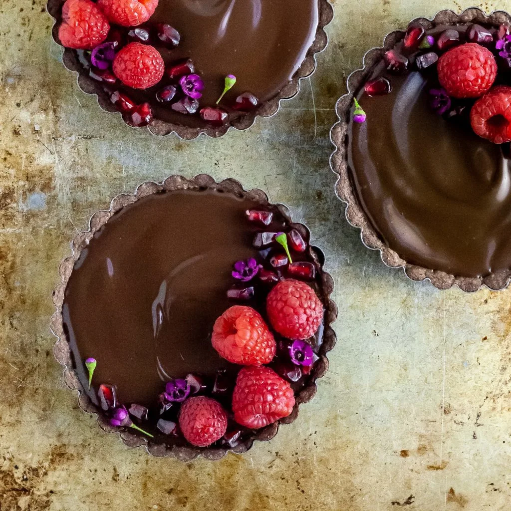 Three Chocolate Raspberry Dream Tarts garnished with fresh raspberries and pomengranate arils