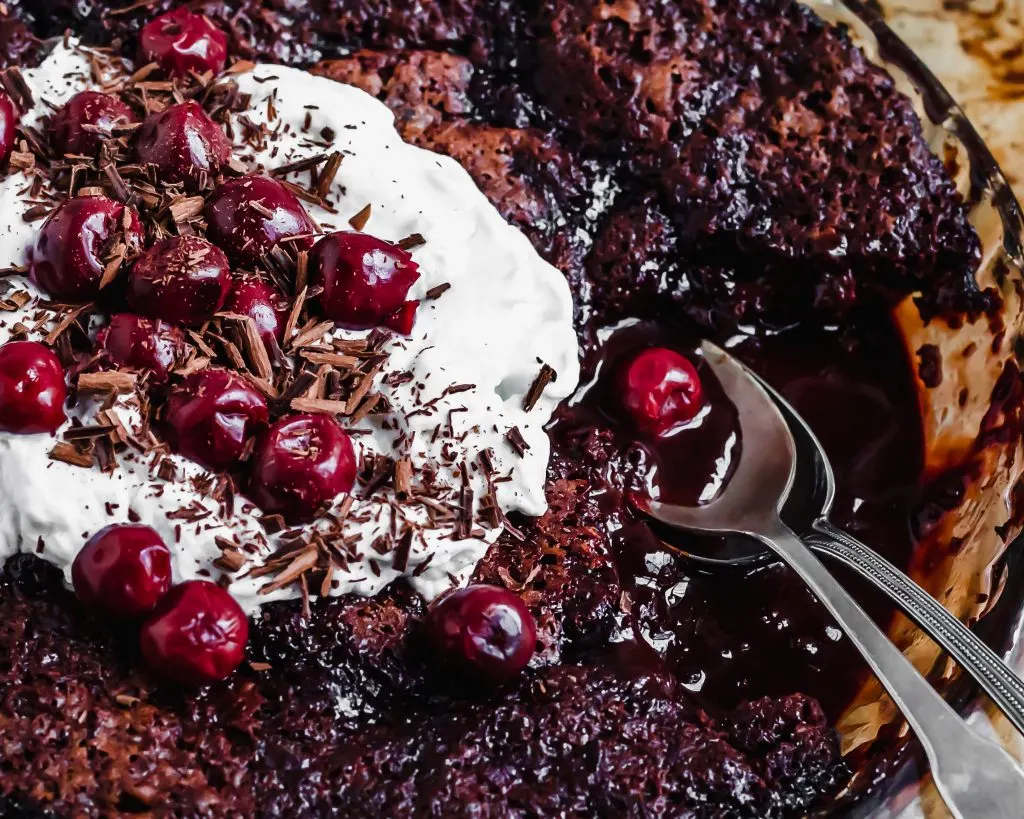 Saucy Cherry Chocolate Fudge Cake close-iup, being served with coconut whipped cream and morello cherries