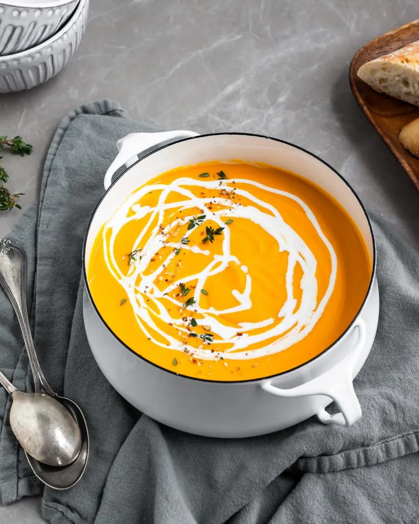 Creamy Curried Carrot, Ginger and Red Lentil Soup in pot with a swirl of coconut milk