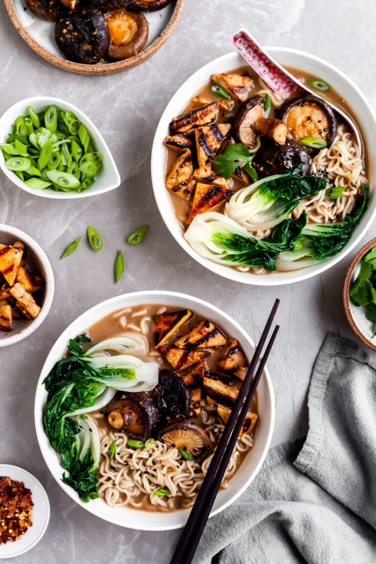 flatlay of 2 bowls of mushroom miso ramen and several bowls of garnishes