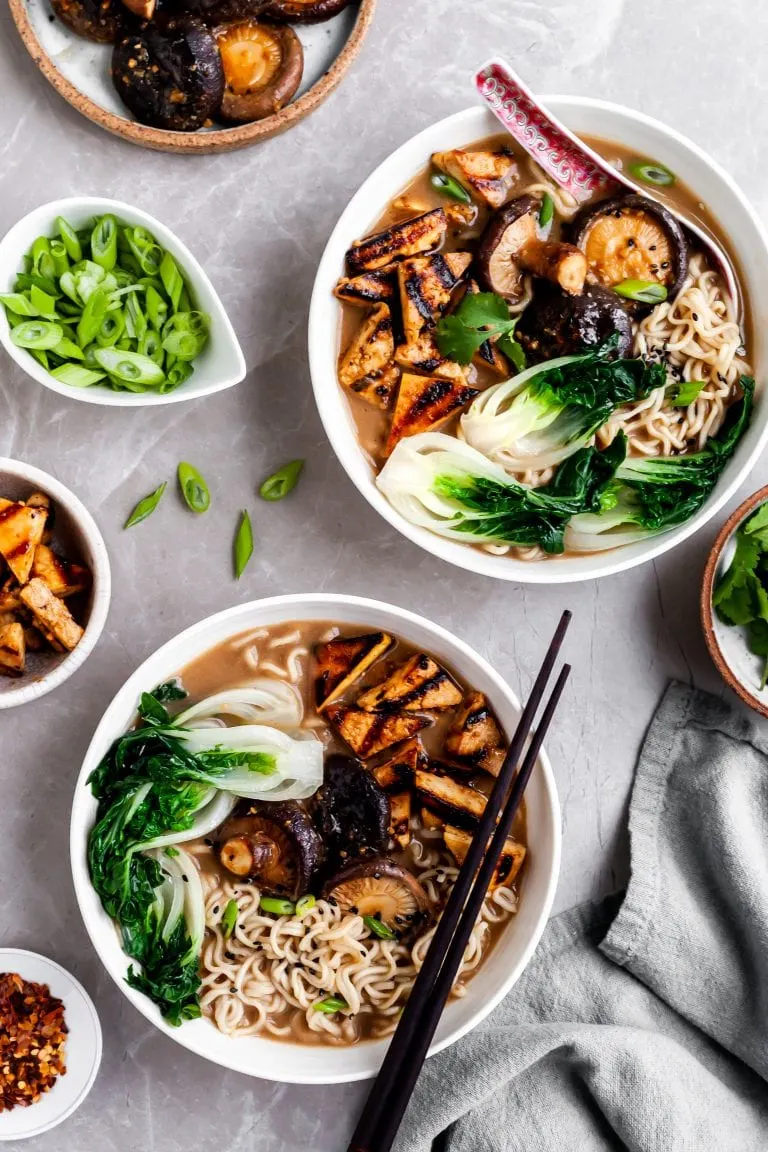 flatlay of 2 bowls of mushroom miso ramen and several bowls of garnishes