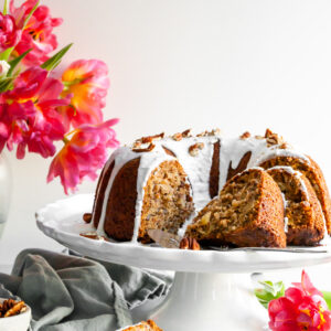 Vegan Hummingbord Cake with Vanilla Glaze sliced and sitting beside a vase of pink tulips