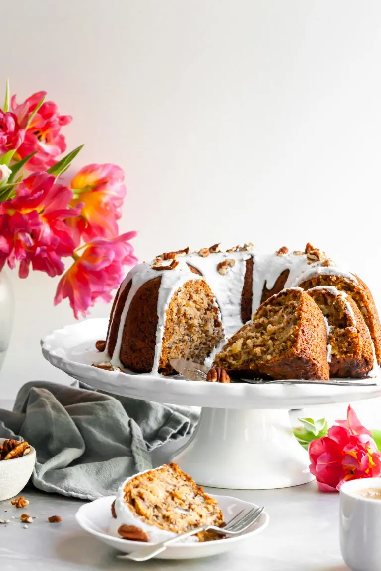 Vegan Hummingbord Cake with Vanilla Glaze sliced and sitting beside a vase of pink tulips