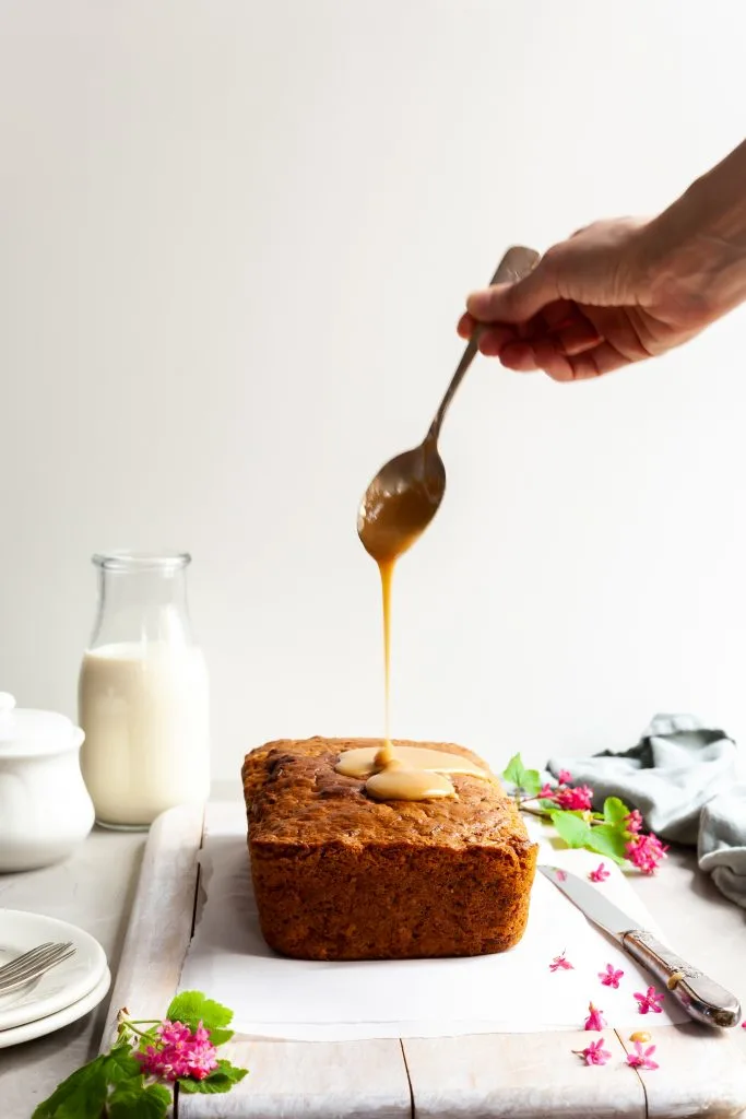 Vegan Carrot Spice Loaf with maple glaze being poured over the top