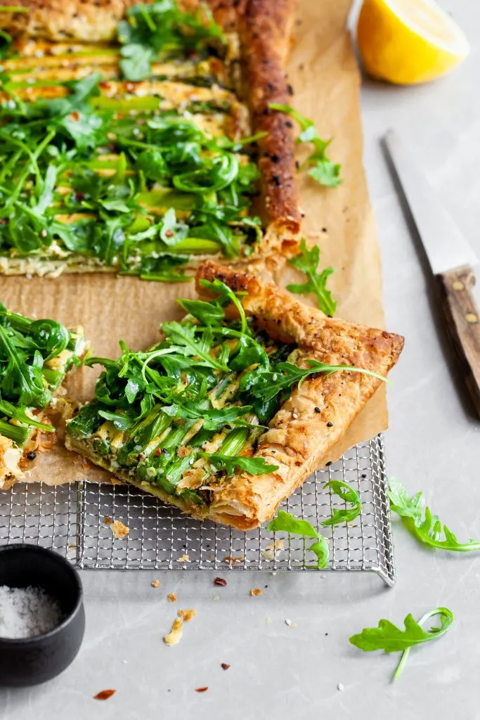Vegan Asparagus and Pesto Cashew Cheese Tart with Lemon Arugula on cooling rack and a close up of one cut slice