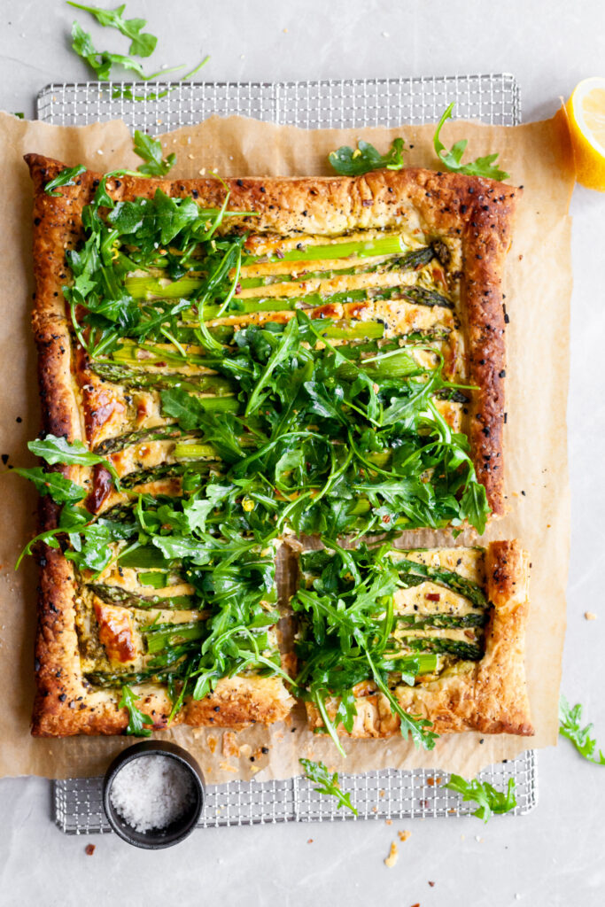 Vegan Asparagus and Pesto Cashew Cheese Tart with Lemon Arugula on cooling rack with one slice cut