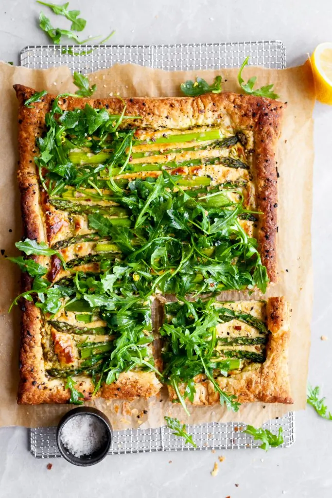 Vegan Asparagus and Pesto Cashew Cheese Tart with Lemon Arugula on cooling rack with one slice cut