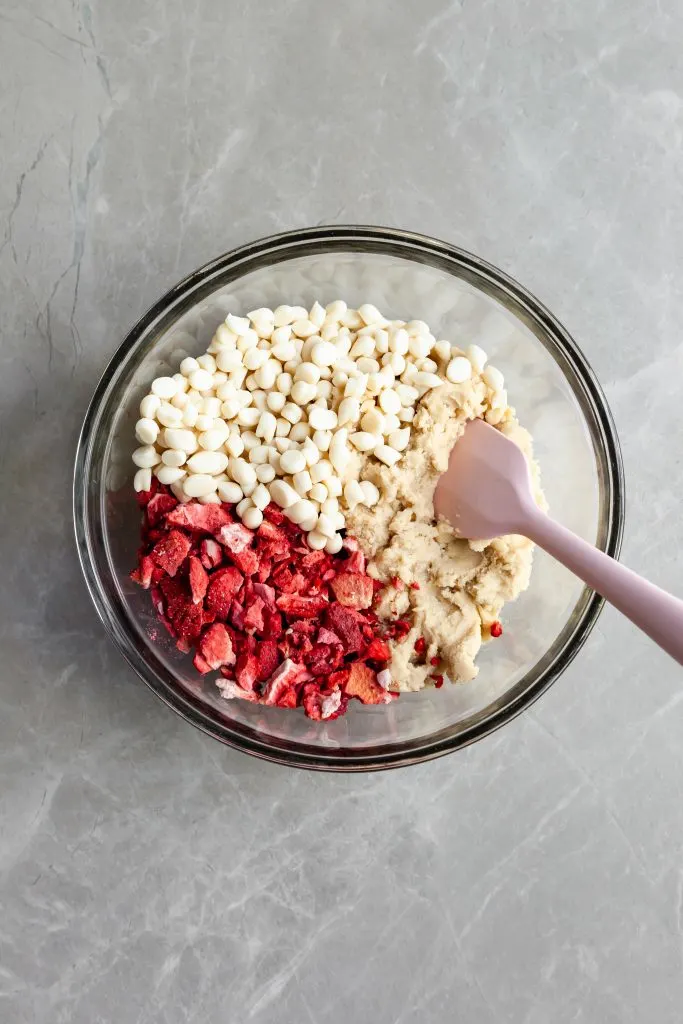 Mixing bowl of cookie dough with freeze dried strawberries and white chocolate chips ready to be mixed in.