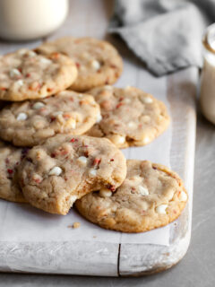 Vegan Strawberries & Cream Chewy Cookies piled on parchment paper with a glass of plant-based milk
