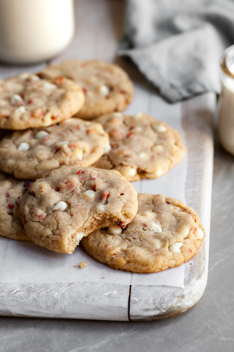 Vegan Strawberries & Cream Chewy Cookies piled on parchment paper with a glass of plant-based milk