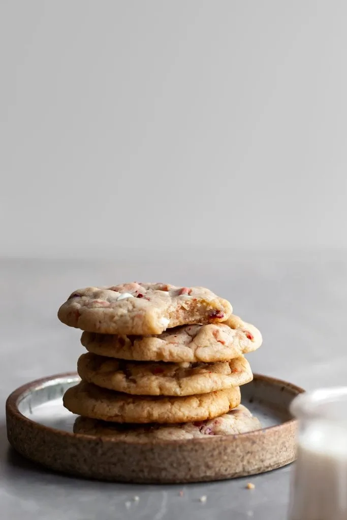 A stack of strawberries and cream cookies on a plate with a glass of plant-based milk in the foreground