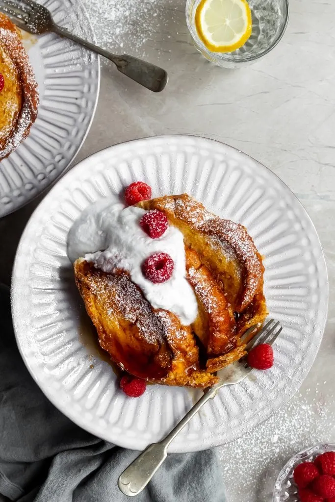Flatlay of a single serving of Overnight Vegan Lemon Raspberry French toast served with vegan cream, fresh raspberries and maple syrup.