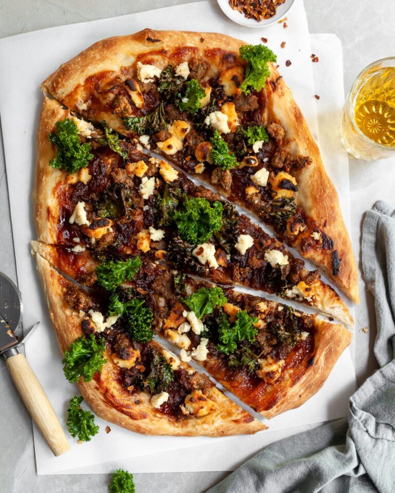 Vegan Caramelized Onion, Sausage and Kale Pizza with Almond Ricotta sliced and served with a glass of beer