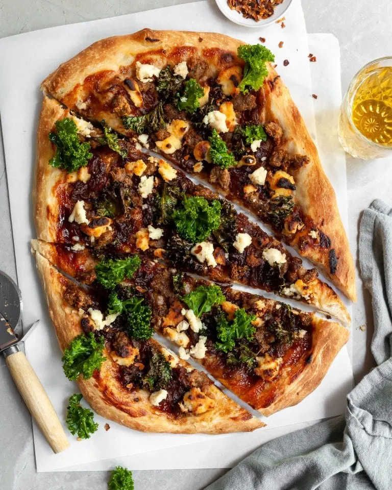 Vegan Caramelized Onion, Sausage and Kale Pizza with Almond Ricotta sliced and served with a glass of beer