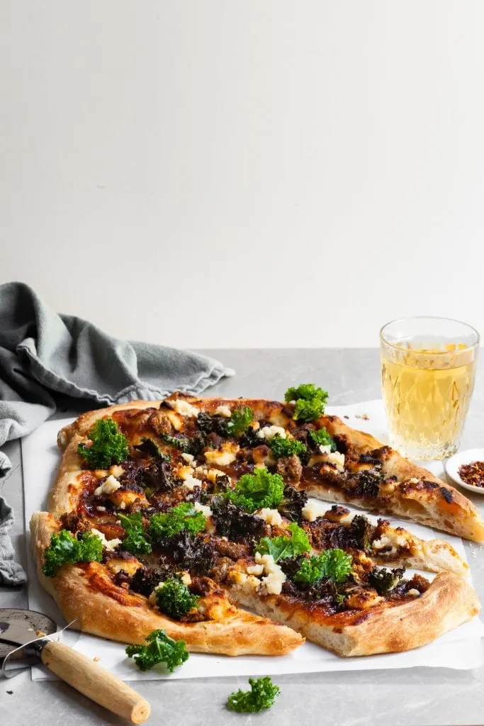 Whole pizza is cut and served with a glass of beer 