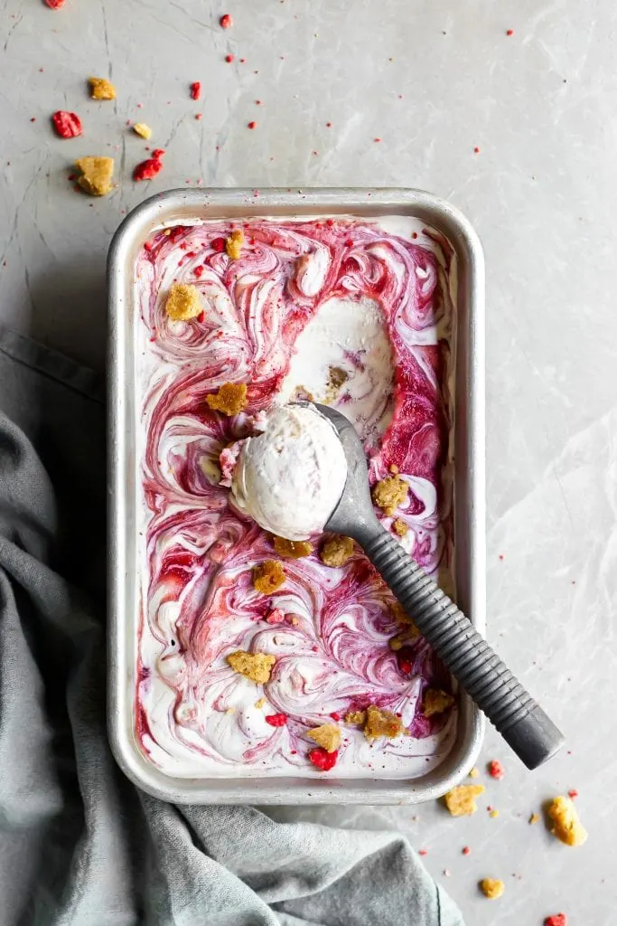 Flatlay of vegan strawberry rhubarb crumble ice cream in loaf pan with one partial scoop just made