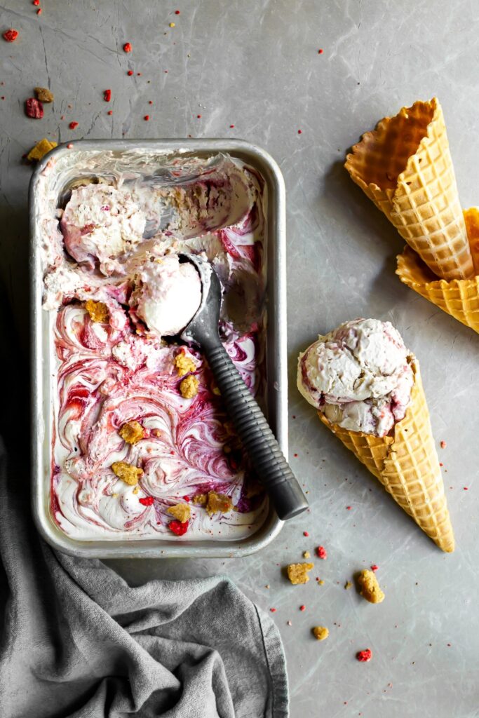 Flatlay of Vegan Strawberry Rhubarb Crumble Ice Cream being scooped from a loaf pan into waffle cones