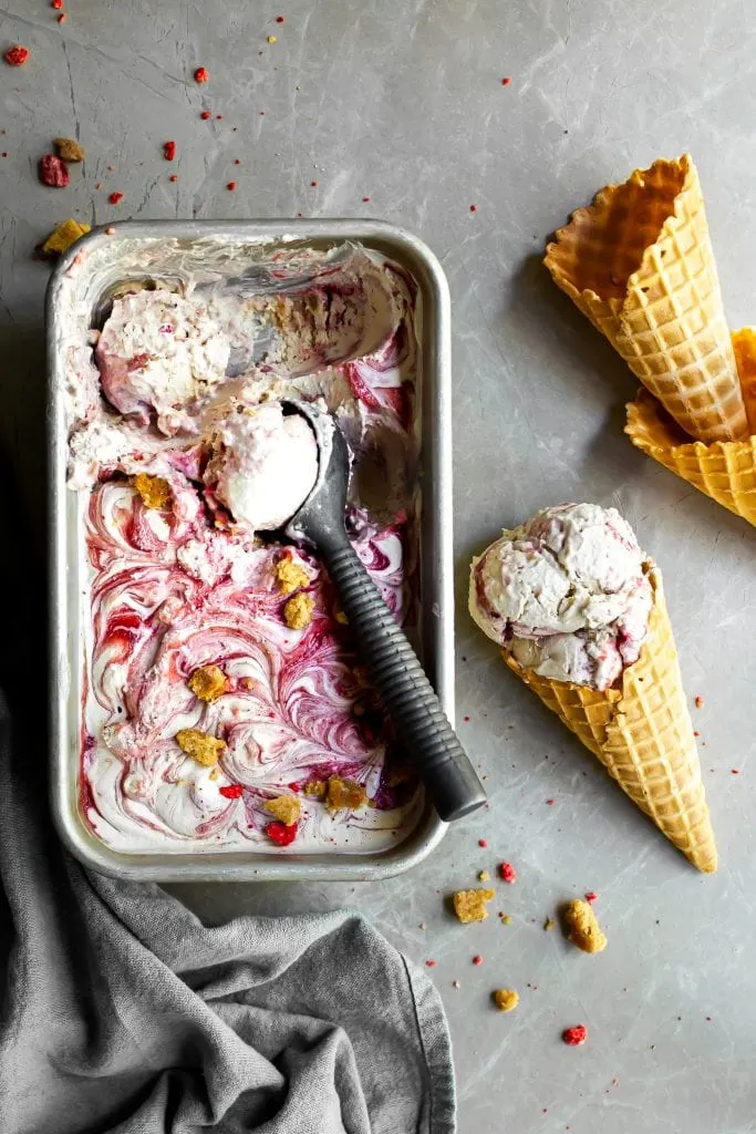 Flatlay of Vegan Strawberry Rhubarb Crumble Ice Cream being scooped from a loaf pan into waffle cones
