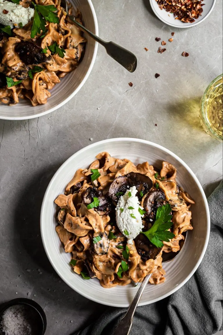 Mushroom Stroganoff served in white bowls, arnished with almond ricotta and parsley