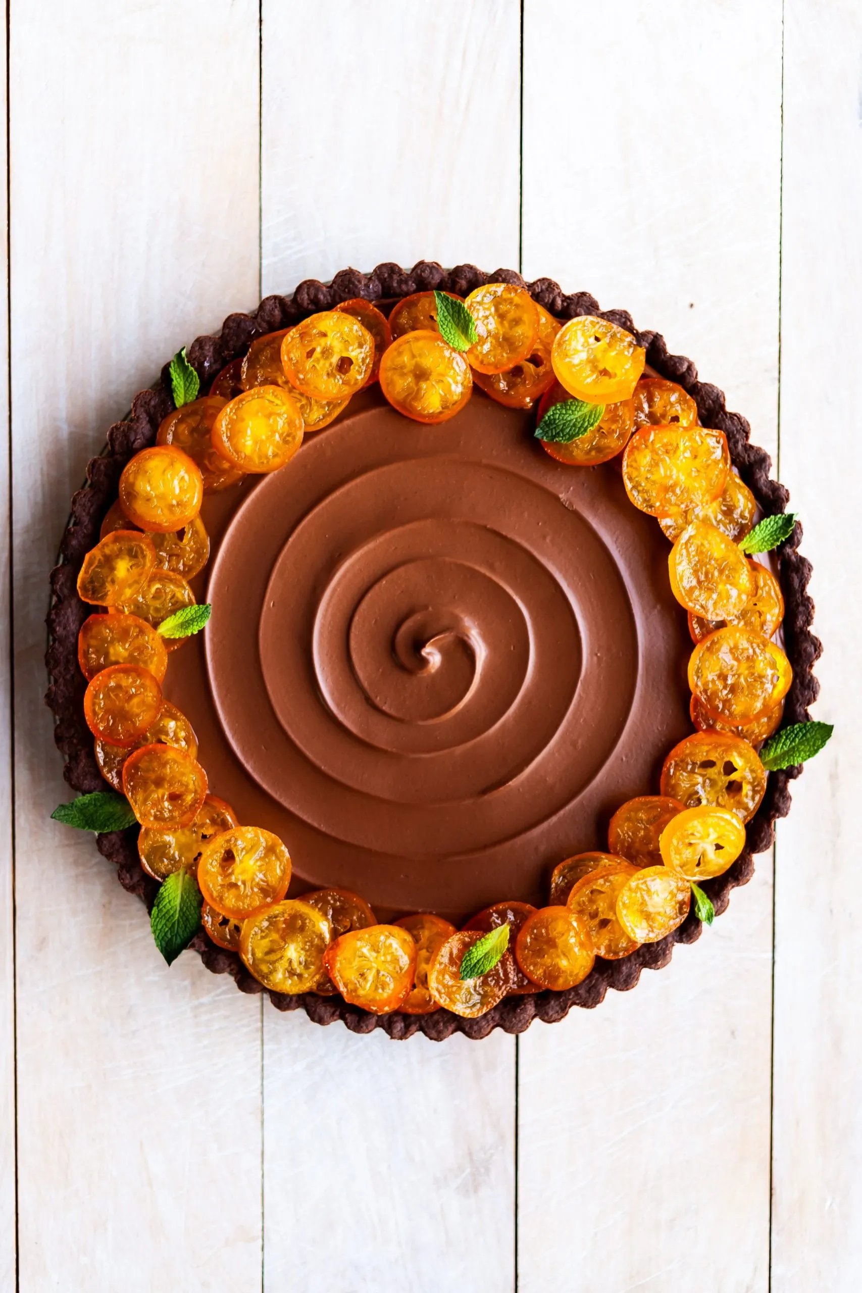 Vegan Chocolate Orange Tart with Candied Kumquats unsliced on a white wood background