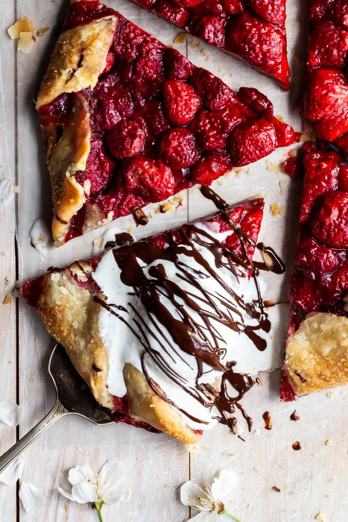 A sliced strawberry galette with one slice being served via a silver spatula. The slice is served with a scoop of ice cream on top, drizzled with chocolate hazelnut spread.
