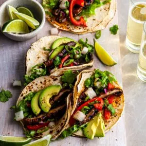 Vegan Korean Tacos served on a white wood board with a side of limes and a glass of beer