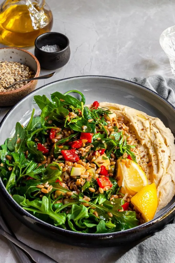 Herby Farro and Grilled Vegetables Salad served over Hummus with fresh lemon wedges and dukkah