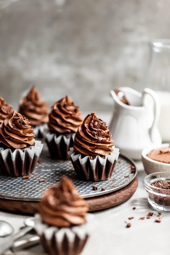 Tray of frosted chocolate cupcakes with chocolate shavings and a jug of plant-based milk