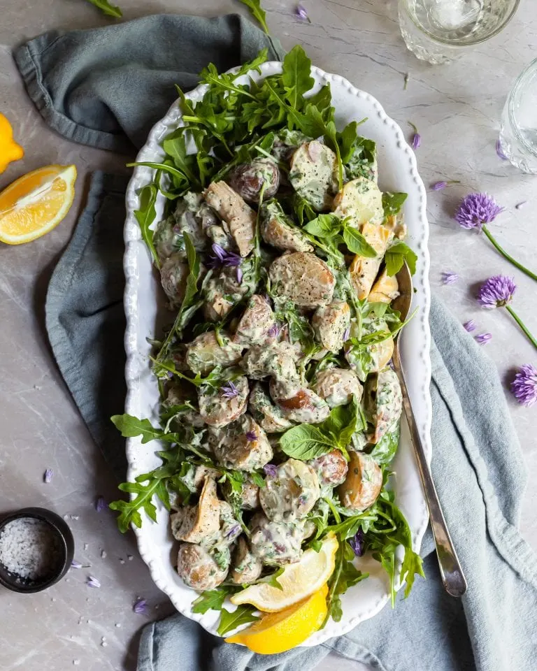 Potato salad on a white platter, garnished with fresh lemons and chive blossoms