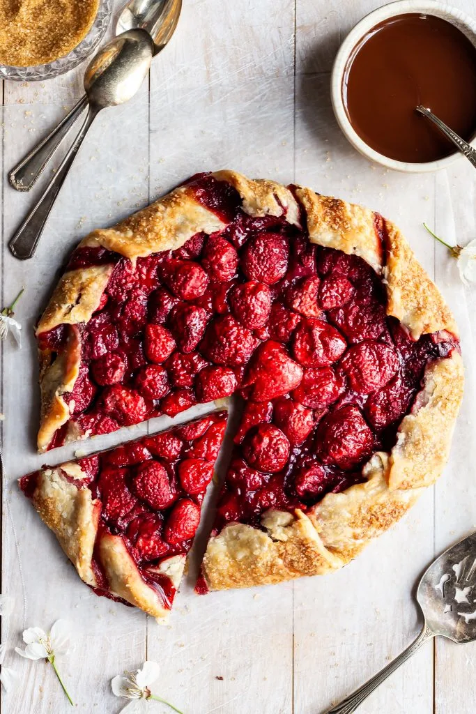 Fresh baked strawberry galette with one slice cut beside a white bowl of chocolate hazelnut sauce