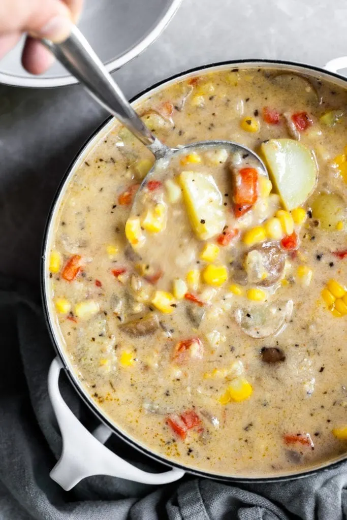 Chowder being ladled from a white pot into a white bowl
