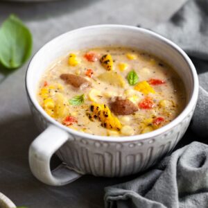 Large mug of chowder on a counter with basil leaves and another bowl in the background