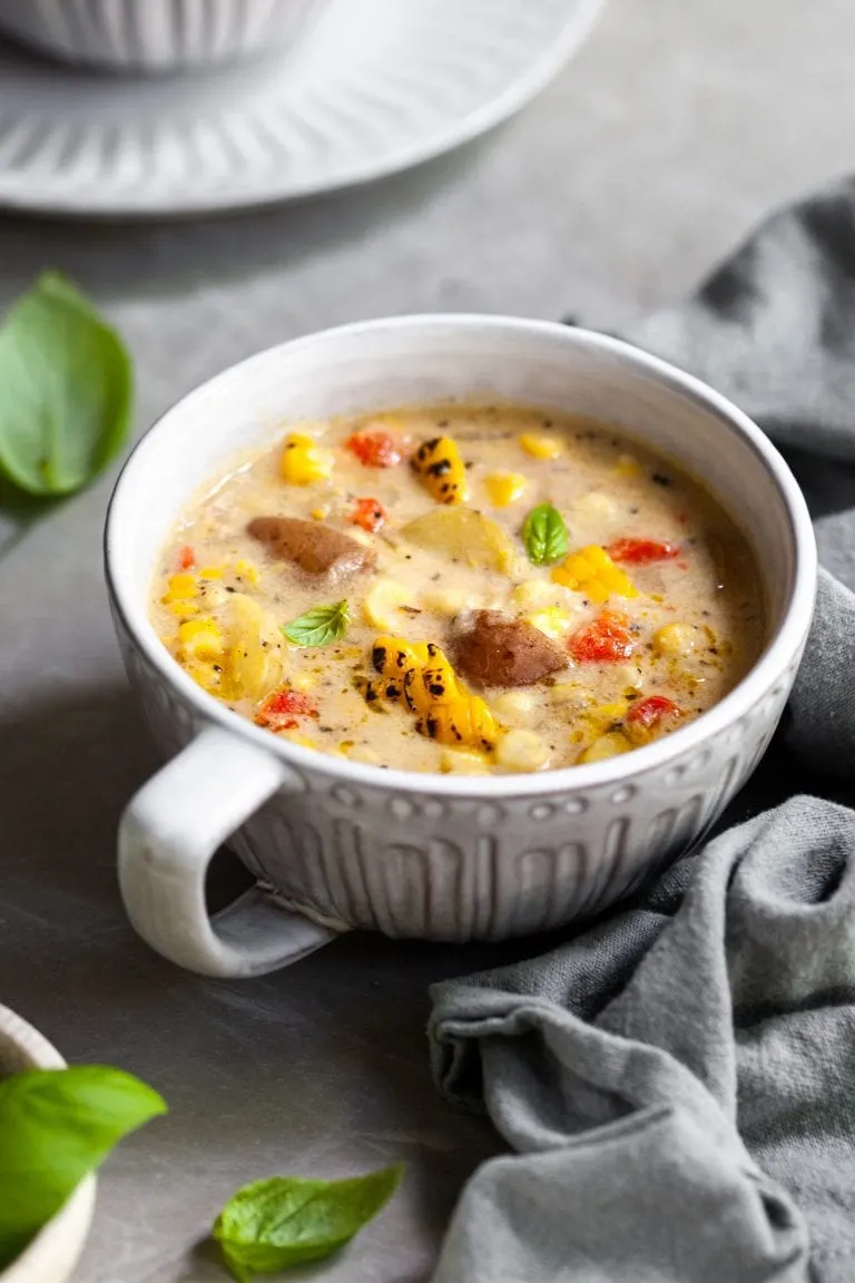Large mug of chowder on a counter with basil leaves and another bowl in the background