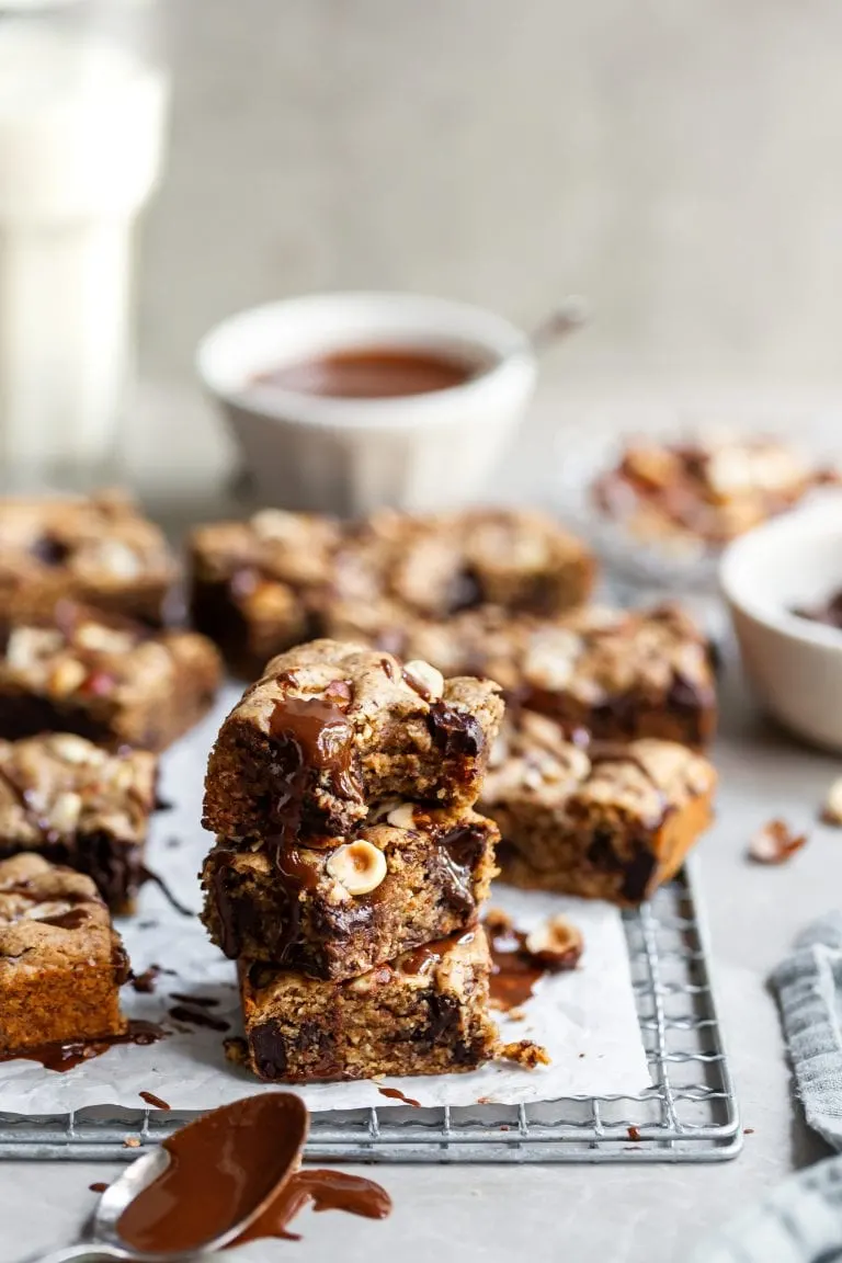 Stack of 3 vegan chocolate chunk blondies with more in the background on cooling rack